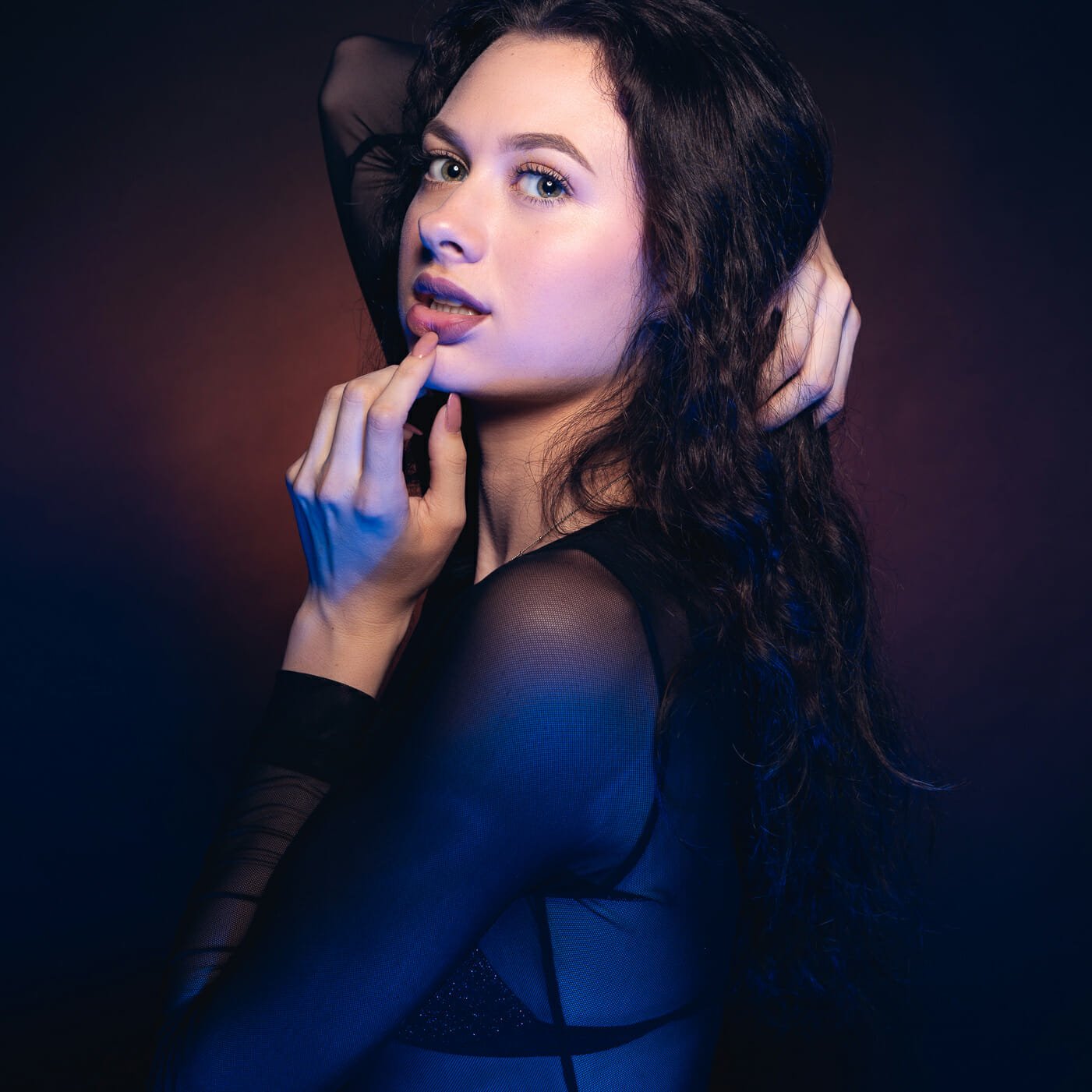 Sarah in studio with a purple / blue gelled setup for lighting. Three quarter shot.